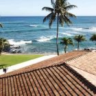 Beachfront view with palm trees and ocean visible from a terracotta-tiled roof.
